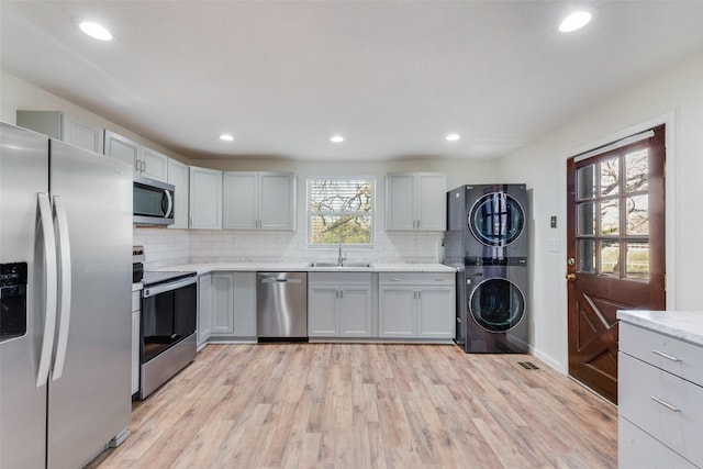 kitchen with appliances with stainless steel finishes, decorative backsplash, sink, stacked washer / drying machine, and light hardwood / wood-style flooring