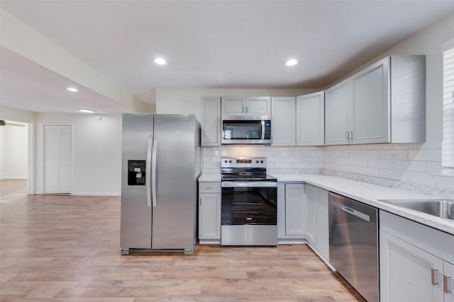 kitchen with gray cabinets, light wood-type flooring, decorative backsplash, and stainless steel appliances