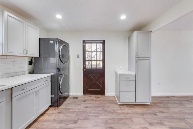 laundry room featuring stacked washer / dryer, cabinets, and light hardwood / wood-style flooring