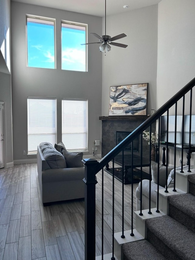 stairs featuring a tile fireplace, a high ceiling, and ceiling fan