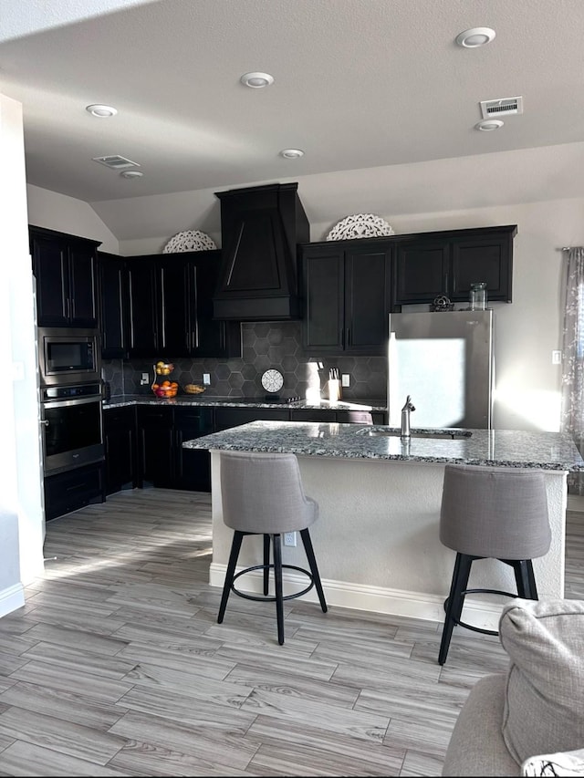 kitchen featuring a kitchen breakfast bar, premium range hood, light stone countertops, and appliances with stainless steel finishes