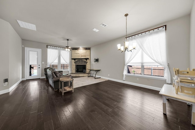 living room featuring ceiling fan with notable chandelier, a stone fireplace, and dark wood-type flooring