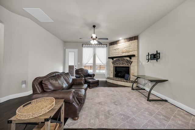 living room with ceiling fan, a skylight, and a stone fireplace