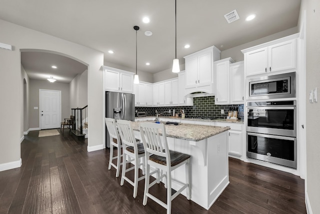 kitchen featuring light stone countertops, white cabinets, decorative light fixtures, stainless steel appliances, and a kitchen island with sink