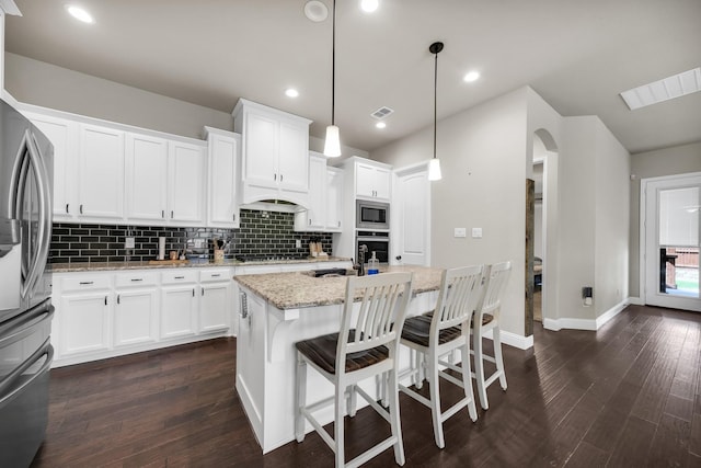 kitchen with pendant lighting, white cabinets, stainless steel appliances, light stone counters, and a center island with sink