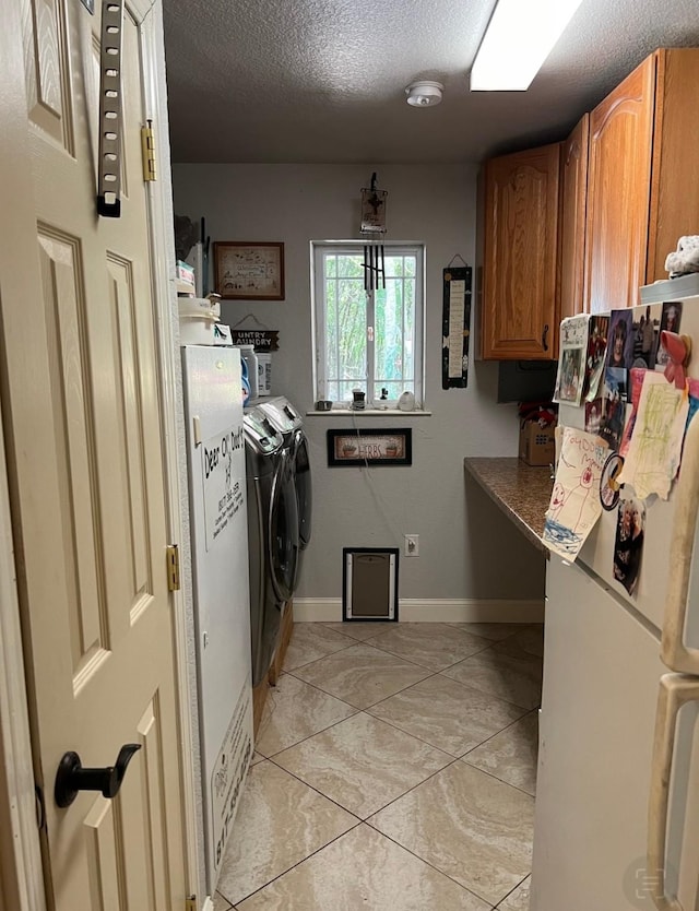 laundry room with cabinets, a textured ceiling, light tile patterned floors, and washing machine and clothes dryer