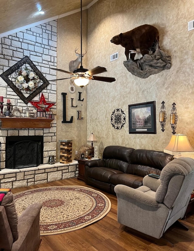 living room featuring a stone fireplace, hardwood / wood-style floors, lofted ceiling, and crown molding