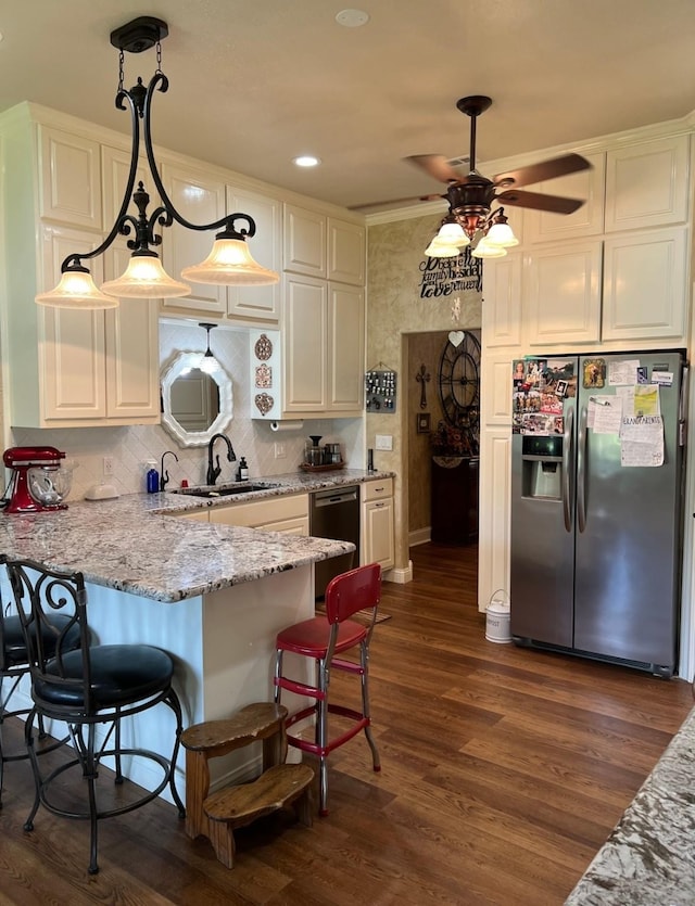 kitchen featuring a kitchen bar, dishwasher, sink, pendant lighting, and stainless steel fridge