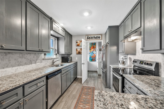 kitchen featuring appliances with stainless steel finishes, sink, light stone counters, gray cabinets, and light hardwood / wood-style floors