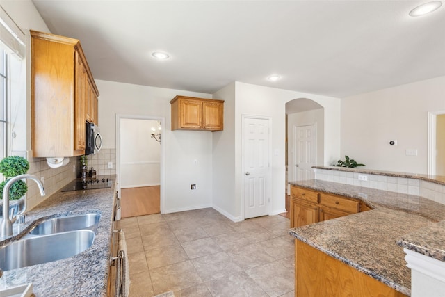 kitchen featuring sink, black electric stovetop, decorative backsplash, kitchen peninsula, and dark stone counters