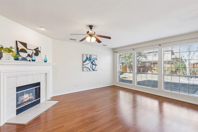 unfurnished living room featuring wood-type flooring, a tile fireplace, and ceiling fan