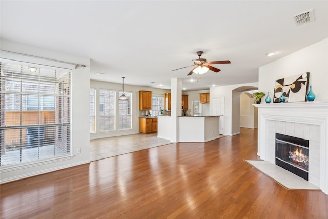 unfurnished living room featuring a tiled fireplace, light hardwood / wood-style floors, and ceiling fan