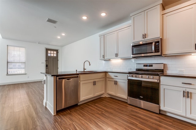 kitchen with appliances with stainless steel finishes, tasteful backsplash, sink, kitchen peninsula, and hardwood / wood-style flooring