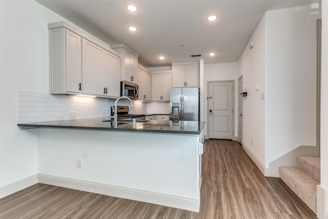 kitchen with kitchen peninsula, appliances with stainless steel finishes, white cabinetry, hardwood / wood-style floors, and decorative backsplash