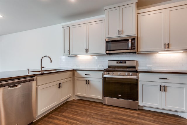 kitchen with appliances with stainless steel finishes, white cabinetry, sink, backsplash, and dark hardwood / wood-style floors