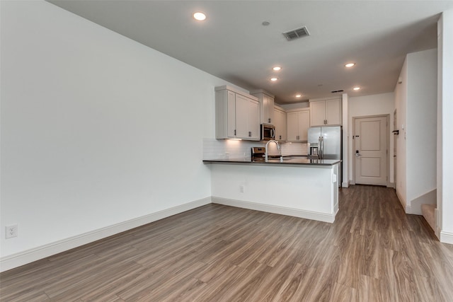 kitchen featuring hardwood / wood-style floors, appliances with stainless steel finishes, white cabinetry, tasteful backsplash, and kitchen peninsula