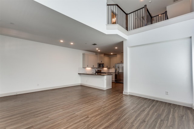 unfurnished living room with sink, a towering ceiling, and dark hardwood / wood-style flooring