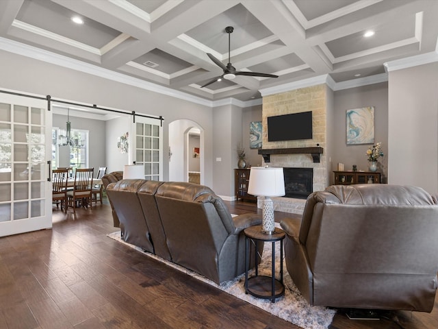 living room featuring crown molding, ceiling fan, dark wood-type flooring, a stone fireplace, and coffered ceiling