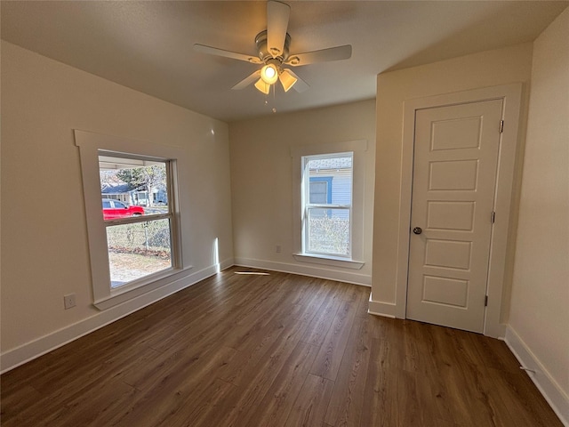 empty room featuring a healthy amount of sunlight, dark wood-type flooring, and ceiling fan