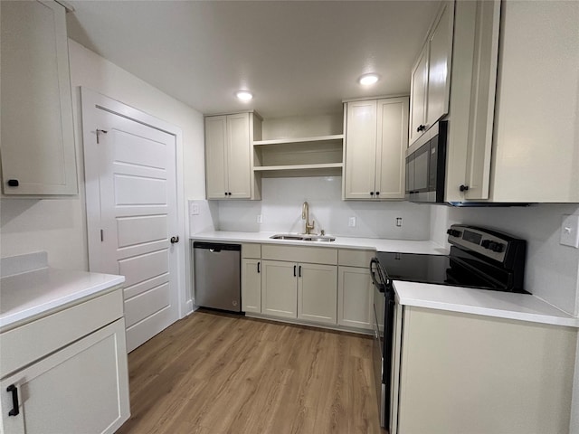 kitchen with appliances with stainless steel finishes, sink, white cabinets, and light hardwood / wood-style flooring