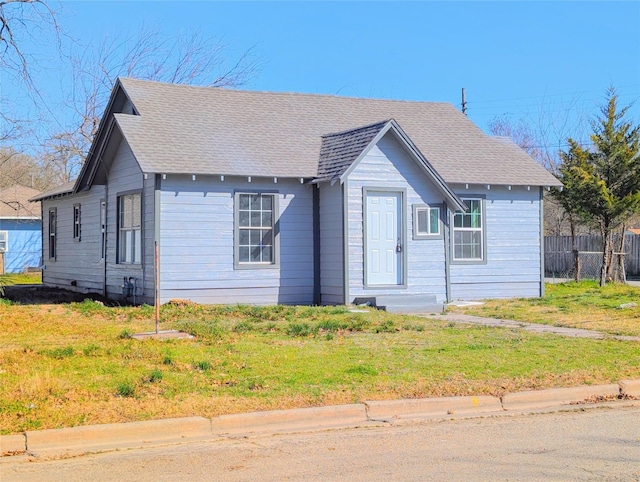 view of front of house with entry steps, a front yard, roof with shingles, and fence