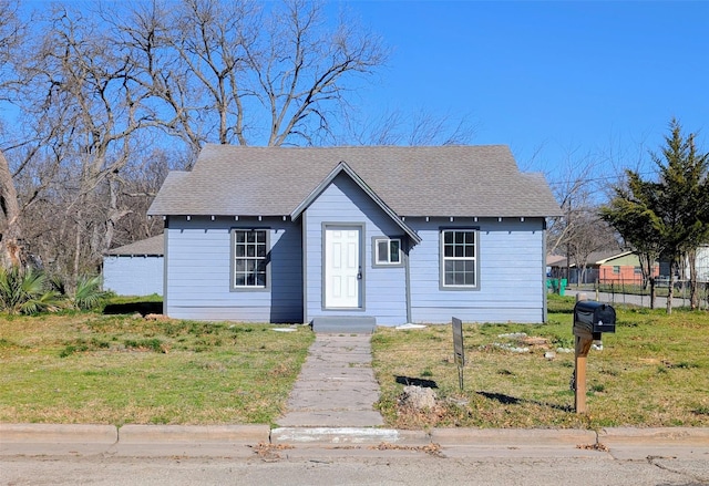 bungalow-style home with roof with shingles, a front lawn, and fence