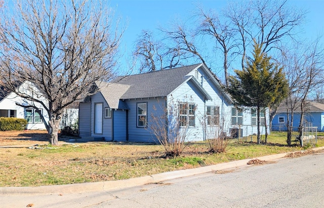 view of front facade with a shingled roof, a front yard, and fence