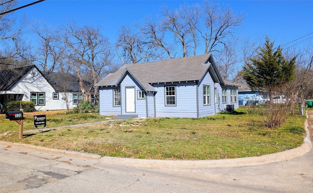 view of front of home featuring central air condition unit, roof with shingles, and a front yard