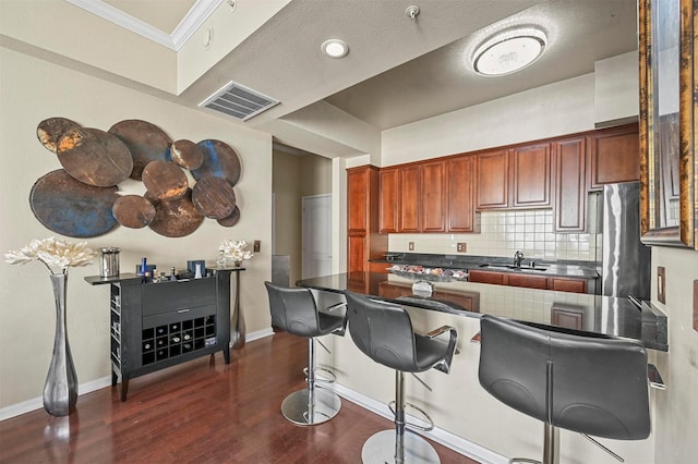 kitchen with tasteful backsplash, stainless steel refrigerator, a kitchen breakfast bar, sink, and ornamental molding