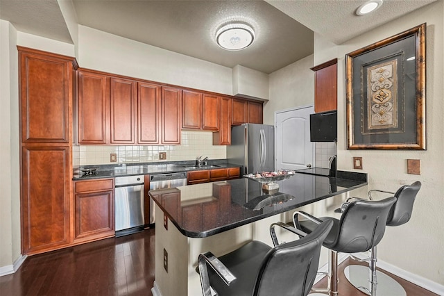 kitchen featuring appliances with stainless steel finishes, sink, backsplash, dark hardwood / wood-style floors, and kitchen peninsula