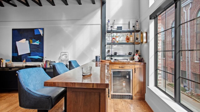 bar with light hardwood / wood-style floors, beverage cooler, and beamed ceiling