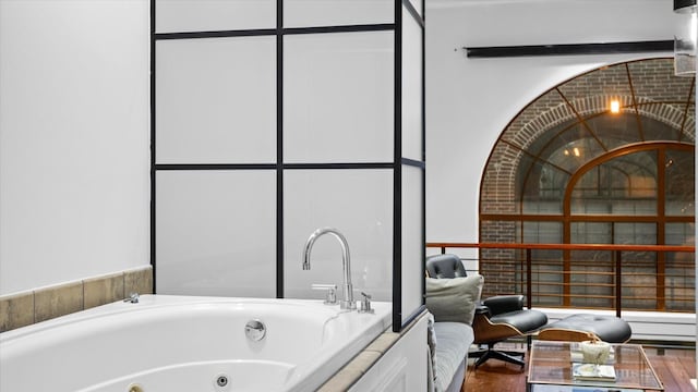 bathroom with a relaxing tiled tub and wood-type flooring