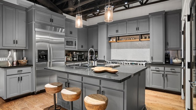 kitchen with gray cabinets, a center island with sink, and built in appliances