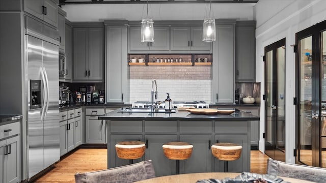 kitchen with light hardwood / wood-style flooring, hanging light fixtures, stainless steel built in fridge, gray cabinets, and a kitchen island with sink