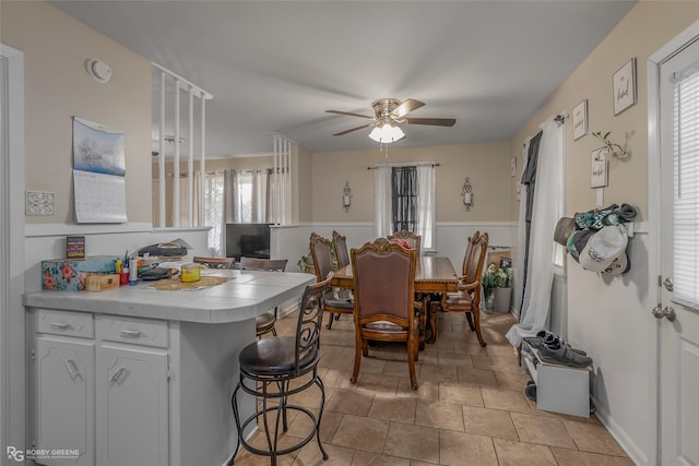 kitchen featuring white cabinetry, a kitchen breakfast bar, kitchen peninsula, ceiling fan, and light tile patterned floors