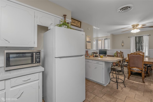 kitchen with kitchen peninsula, white refrigerator, a breakfast bar area, and white cabinetry