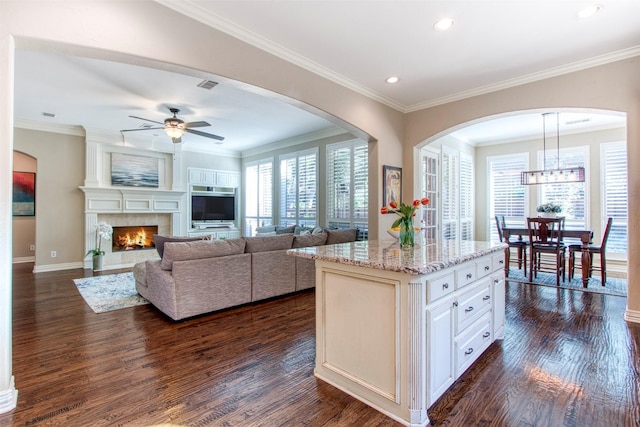 kitchen featuring dark hardwood / wood-style floors, pendant lighting, a large fireplace, a center island, and light stone countertops