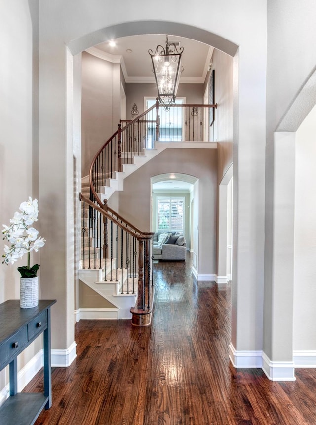 foyer with crown molding, a towering ceiling, dark hardwood / wood-style floors, and an inviting chandelier