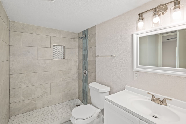 bathroom featuring a textured ceiling, toilet, vanity, and tiled shower