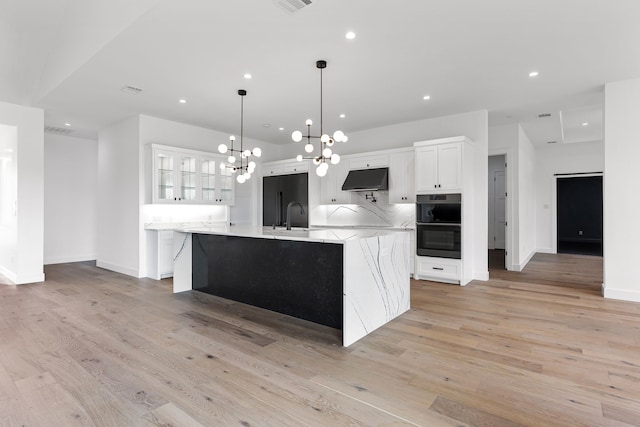 kitchen featuring white cabinetry, a large island, sink, light wood-type flooring, and pendant lighting