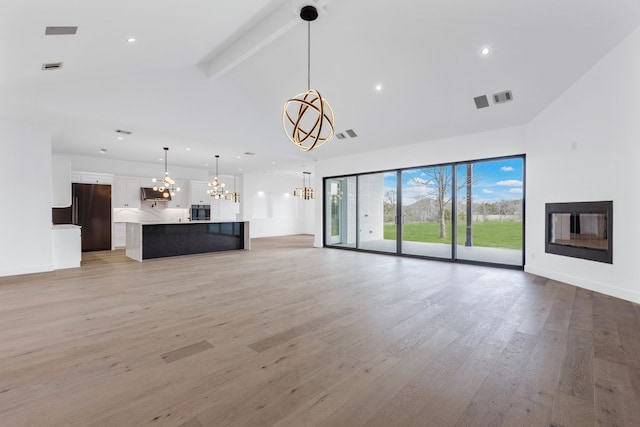 unfurnished living room with vaulted ceiling with beams, light hardwood / wood-style flooring, and an inviting chandelier