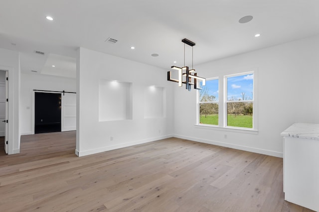 unfurnished dining area featuring an inviting chandelier, a barn door, and light wood-type flooring