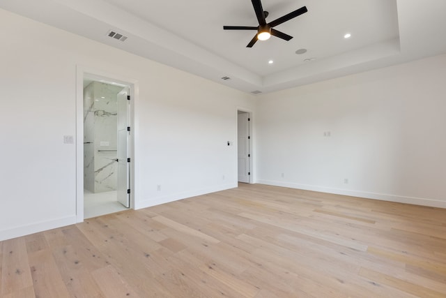 unfurnished room with light wood-type flooring, ceiling fan, and a tray ceiling