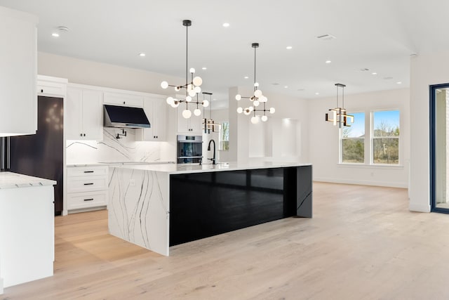 kitchen featuring decorative light fixtures, white cabinetry, a large island with sink, and decorative backsplash