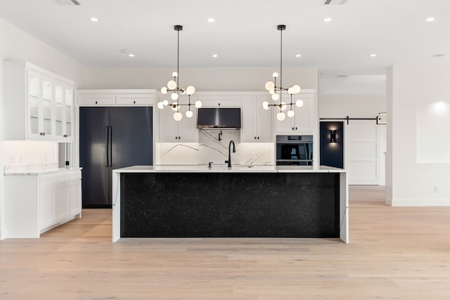 kitchen with black refrigerator, white cabinetry, a barn door, pendant lighting, and a center island with sink