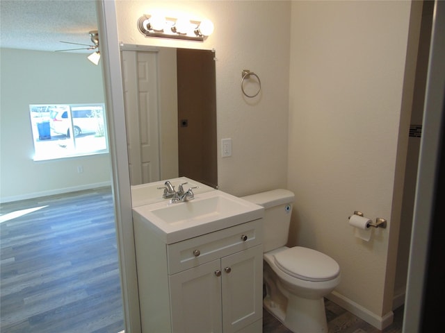 bathroom with ceiling fan, vanity, wood-type flooring, a textured ceiling, and toilet