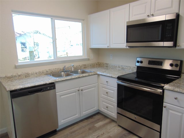 kitchen with light stone countertops, appliances with stainless steel finishes, white cabinetry, light hardwood / wood-style floors, and sink