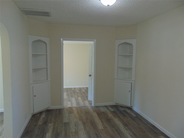 unfurnished room featuring built in shelves, dark hardwood / wood-style floors, and a textured ceiling