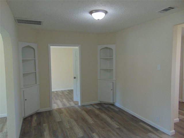 unfurnished room with dark wood-type flooring, built in shelves, and a textured ceiling