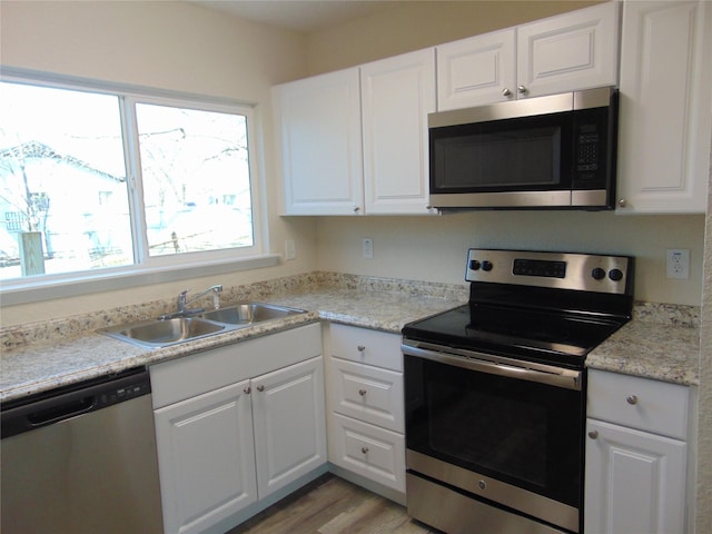 kitchen featuring sink, white cabinetry, light stone counters, appliances with stainless steel finishes, and light hardwood / wood-style floors